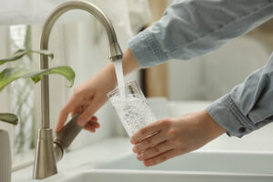 Woman filling glass with water from tap at home, closeup